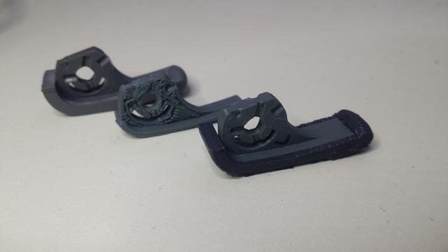 An original grey rotating foot and the prototypes in front of it, resembles a little foot with a hole in the ankle. The front version has an external TPU shell that's a little darker, since the original had 2 different plastics.