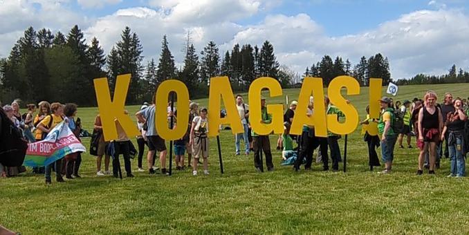 Menschen auf der Wiese vor dem Gelände des Gaskonzerns halten große gelbe Buchstaben hoch. Zu lesen ist der Text "KoaGas!"