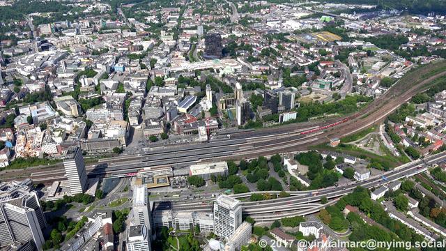 An aerial photo of the Essen central station towards the city center. There is a big black building in the top middle, which is the city hall. In the bottom is a big freeway, the A40 (called the "Ruhrschnellweg"/Ruhr expressway).