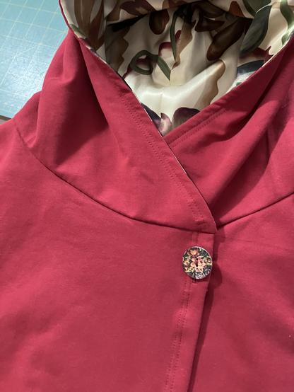 Close up view of the buttoned burgundy fleece hoodie, showing the printed ivory floral silk hood lining.