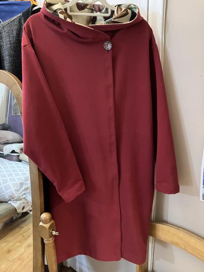 View of full length burgundy fleece asymmetrical hoodie with single button closure near neckline and floral printed hood lining