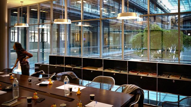 Une salle de réunion, une personne en conversation avec quelqu'un hors champ sur la gauche, et un lobby végétalisé d'immeuble parisien un peu snob en arrière plan.