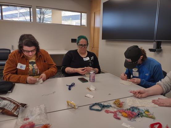 Another three humans embroidering, with a pile of thread on the table