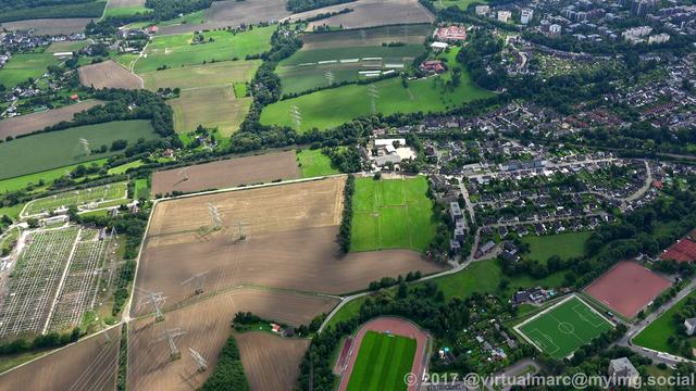 An aerial photo of a border region between essen and bochum. The right side of the image is Essen with small houses and some living quaters in the green. On the left are farm yards and a big Electrical substation.