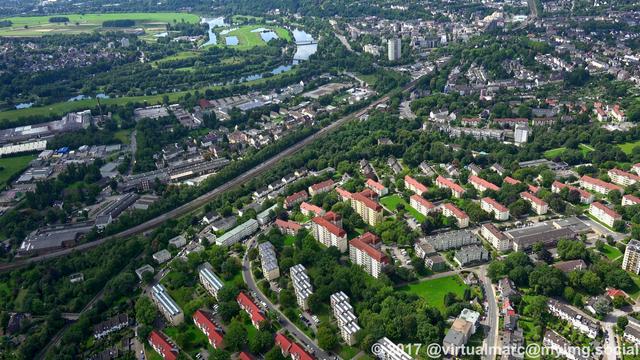 An aerial photo of living quarters in Essen with trees all around. You can see a river, the ruhr, at the top left.