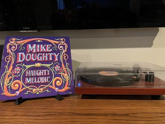 A picture of a record sleeve standing up and to the right of it is my record player.  The album sleeve says Mike Doughty in big letters and under that it says Haughty Melodic.  To the right, my record player sins a black record.