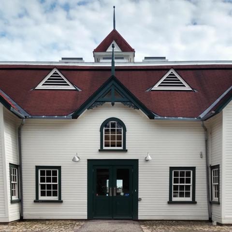 Grand heritage farm house with white wood siding, green trim windows and red roof.