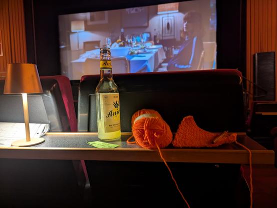 Foto zur Leinwand mit Getränk, Wollknäuel und Häkelnadel im Bild. Links eine kleine Tischlampe.
