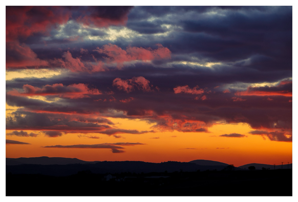 Fiery embers of a sunset with distant hills silhouetted against a dark golden sky.