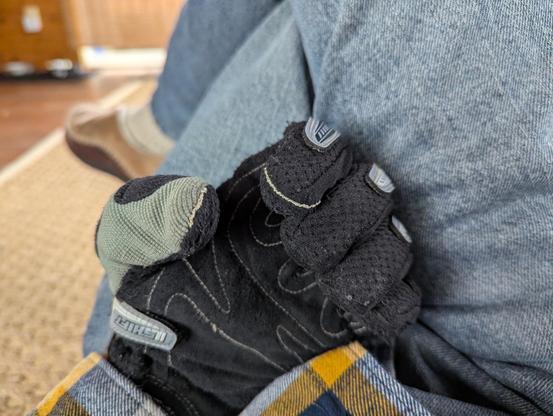A photo of a pair of black mechanic's gloves on a hand. The palm is facing the camera and the fingers and curled to show the tips. The thumb and index finger have silver conductive thread stitched into the seam at the tips, in order to allow the user access to their touchscreen phone.