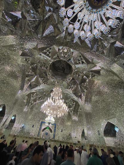 Inside of one really large room or hall of Imam Reza shrine. The walls and ceiling are made of mirror mosaique and there are two huge chandeliers.