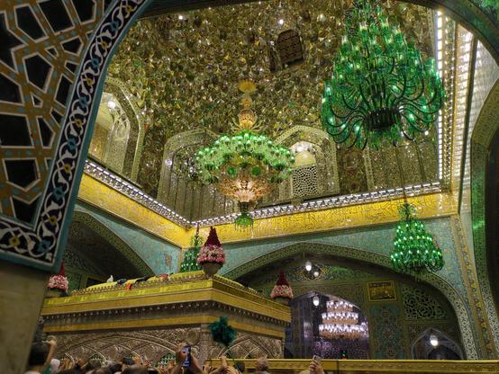 The room of Imam Reza's tomb. There are green chandeliers and the walls are colourful anf greenish shiny with all those mirror mosaique. In the middle of the room there is a huge cube, in that one is his tomb.