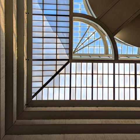 A skylight shot looking straight up. There are balconies to the left and right as vertical and horizontal lines contrasting the skylight's semi circular angles.