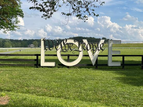 White LOVE sign with “We the People” in black calligraphic script along the top.