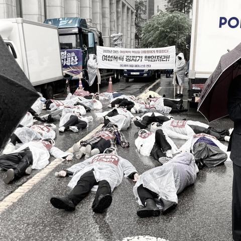 폭우가 쏟아지던 노동절, 다이인 퍼포먼스를 하는 젠더폭력 해결 페미니스트 연대. 우비를 입은 사람들이 비가 내리는 도로에 누워있다. 이 퍼포먼스는 여성폭력으로 사망한 사람들을 상징한다.