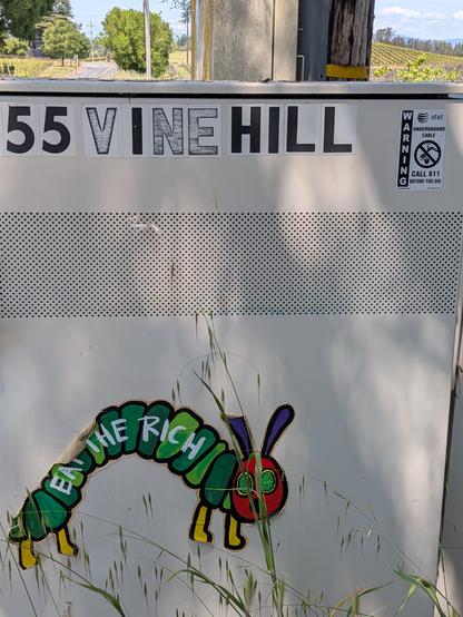 An electrical panel box with Carle's Hungry Caterpillar on it, like graffiti I mean, and on that (it's peeling) "EAT THE RICH"