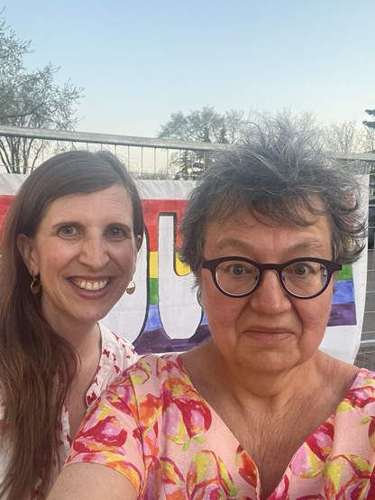 Edmonton City Councillor Anne Stevenson and Senator Simons snap a selfie in front of a rainbow banner.