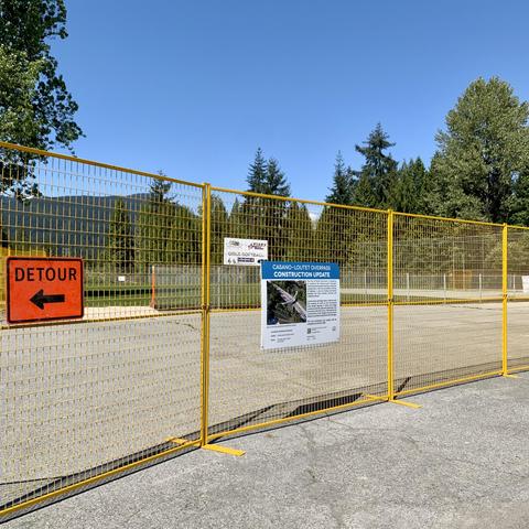 Yellow construction fence at the southwest end of the overpass project. The fence has an information sign about the project on it.
