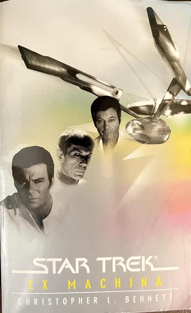 Cover of the TOS novel Ex Machina (2004) by Christopher L. Bennett, showing Kirk, Spock, and McCoy in the TMP era with the Enterprise refit behind them with a jagged shape and pastel greens, yellows, reds, and pinks below and to the left and right of the ship.