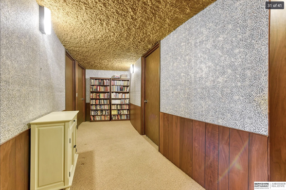 A hallway with the ceiling covered in mustard coloured shag carpet with panels on the walls and a bookshelf at the end of the hallway