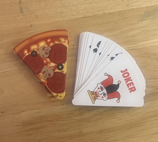 Photo of playing cards. They are wedge shaped and look like a slice of pizza on the back. The toppings are (presumably) vegan cheese, pepperoni, mushrooms, and black olives.