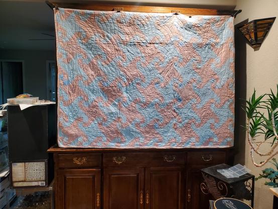 A pink and blue quilt hanging from the back of a bookshelf dividing a room in half.