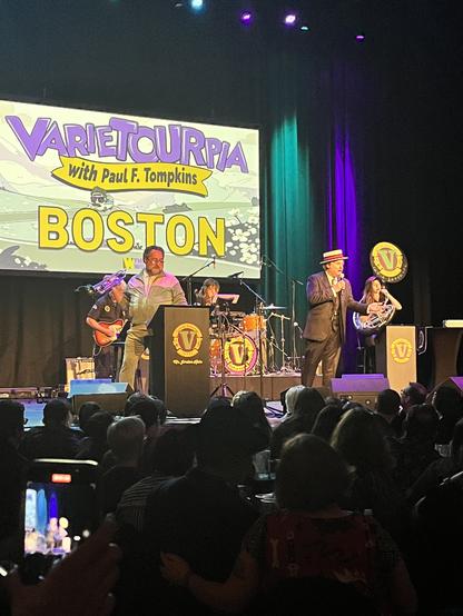 PFT on stage wearing a top hat and singing. Band behind him.