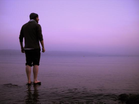 A person stands on a lake shore in the purple glow of last light