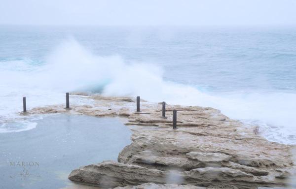 Es sind flache Felsen zu sehen die ins Meer zeigen und von der Brandung überspülz werden. An einer Felsenseite sind Pfosten zu sehen und ein Naturpool auf der linken Seite. Weiße Wellen überpülen diese und spritzen hoch. Die Szenerie ist sehr hell gehalten, die Wellen weiß.
AI disclaimer: Using my work, its meta , written or derived description to create media with or train AI based systems is prohibited.