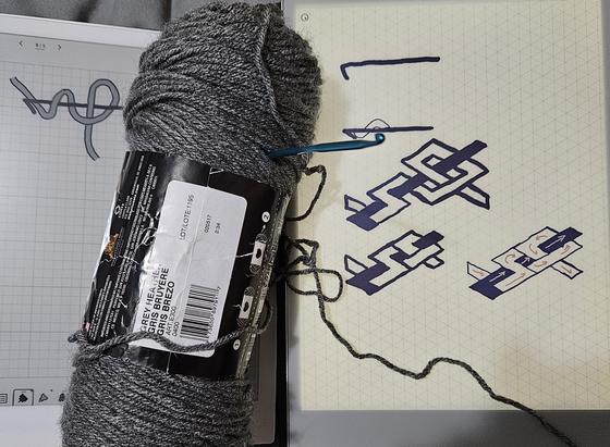 2 eink tablets and some yarn with a needle poking out. the tablets depict the first step in a pattern for making spherical shapes.
