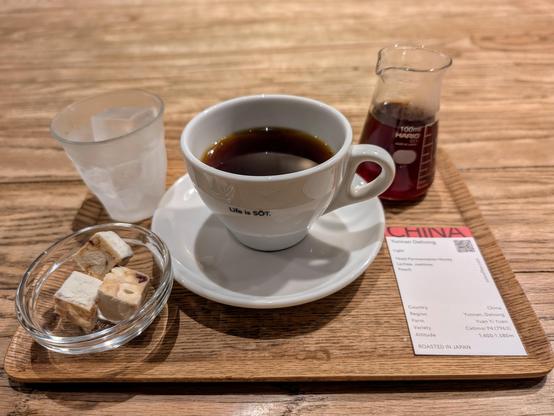 A cup of hot coffee, a beaker with more coffee, a glass with ice and a couple of pieces of toffee.