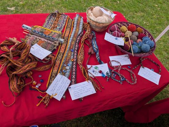 Table covered with woven bands and straps and current projects, a basket filled with colorful balls of yarn, and a basket of white cotton - carded and spun.