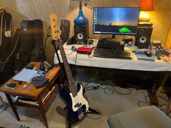 Fender Precision bass guitar on stand in basement with computer and miscellaneous music gear