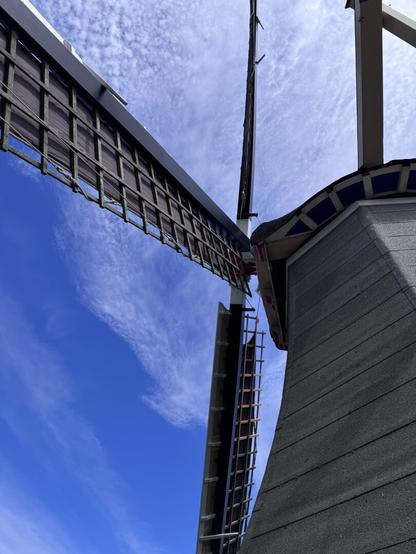 The sails of a windmill against a blue sky with wispy clouds