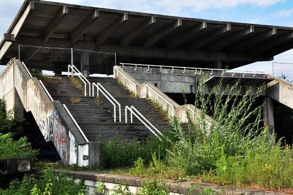 Ein ungenutzter S-Bahnhof aus den 1970ern. Viel Beton. Die Bahnsteige und Treppen sind von Pflanzen überwuchert. Überall Graffiti.