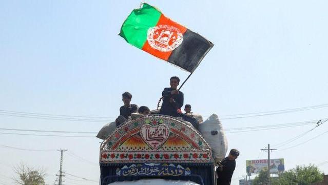 Un nen fa onejar una bandera de l'Afganistan mentre torna a l'Afganistan juntament amb la seva família dalt d'un camió (Fayaz Aziz (Reuters))
