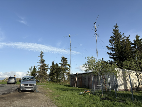 A car, a couple of garages and amateur radio yagi antennas in front of trees.