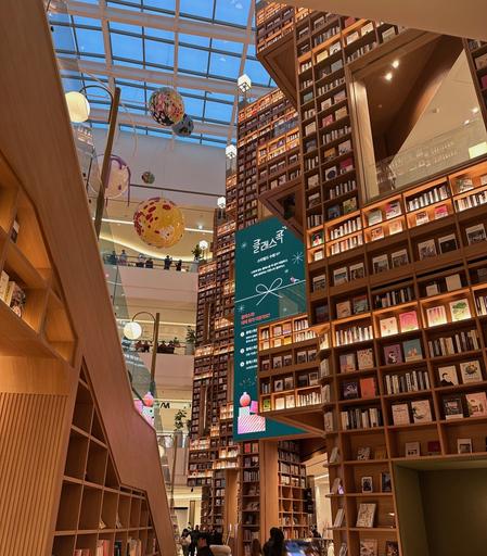 Walking into the main library area from the side. There are high bookshelves rising up on the right, while on the left is the main tiered benches/steps.