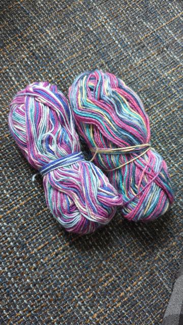 Two yarn balls side by side. It's self-patterning sock yarn mostly in pink/violet tones.