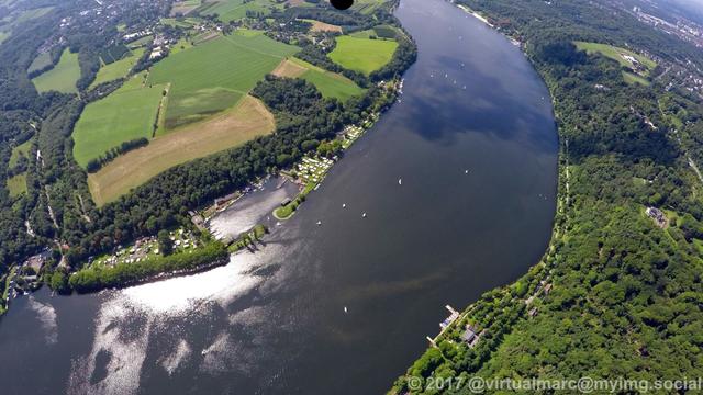 An aerial photo of the part where the ruhr river becomes the Baldeneysee, with some sailing boats on it, sourrounded by woods and farm yards.