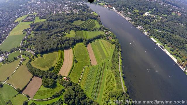 An aerial photo of the part where the ruhr river becomes the Baldeneysee, with some sailing boats on it, sourrounded by woods and farm yards.
