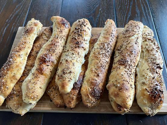 Auf einem dunklen Holztisch liegt ein Holzbrett. Darauf liegen zahlreiche frisch gebackene Brötchen mit rustikalem Ausbund.