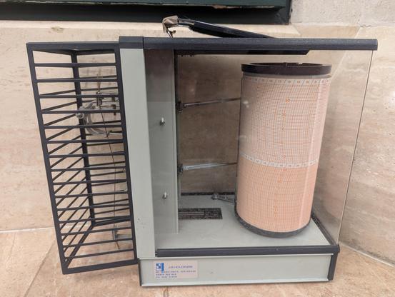 An old style cylindrical humidity recorder device. It plots humidity on a rotating paper chart.