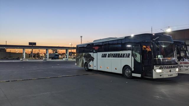 A mainline bus on a huge parking orange sunset light.