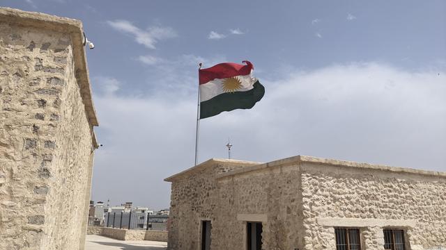 A Kurdistan flag waving above the roof of a fortress.