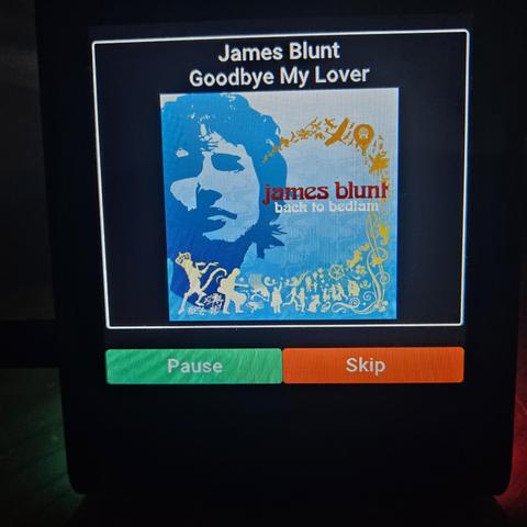 A Small colour screen showing the album art of James Blunt Back to bedlam with the track and artists name. There are two buttons along the bottom for Pause and Play