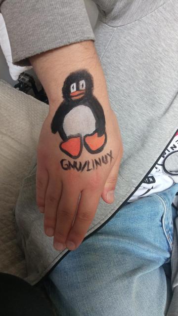 Malunek maskotki Linuxa z podpisem "GNU/Linux" na dłoni