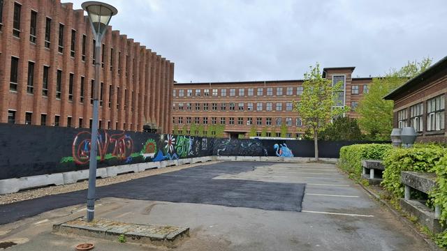 We are standing in the afternoon rain in a section of the grounds of the huge former Aarhus Amtssygehus (County Hospital) that was used from 1883 to 2018. It is near the city centre here in Aarhus, Denmark. To our left: a bombastic four-storey red-brick building with lots of windows – a later addition in the 1970s. Beyond: one of the original buildings from the late 1880s whose architecture is world-famous in Aarhus: red brickwork with single rows of yellow bricks, like ribbons, under the row of windows for each storey. To our left, a black construction work hoarding with colourful street art painted on it. To our right, a low green hedge and a few trees in front of a low building. In front of us, a single lamp-post on a messy grubby patch of ground covered in building dirt and dust. A large section of it is covered in a T-shaped patch of tarmac, haphazardly filling in, temporarily, the holes from which cranes lifted out the two generators that still worked in the underground bomb-proof hospital rooms built after the second world war. The respectively 380 kVA and 750 kVA generators were donated by Aarhus Kommune (council) and construction company developer Raundahl & Moesby to Ukraine. Danish charity group Generators For Ukraine transported them to a hospital in Odessa that treats both civilians and frontline soldiers. It had previously been hit by power cuts of up to 8 hours a day.