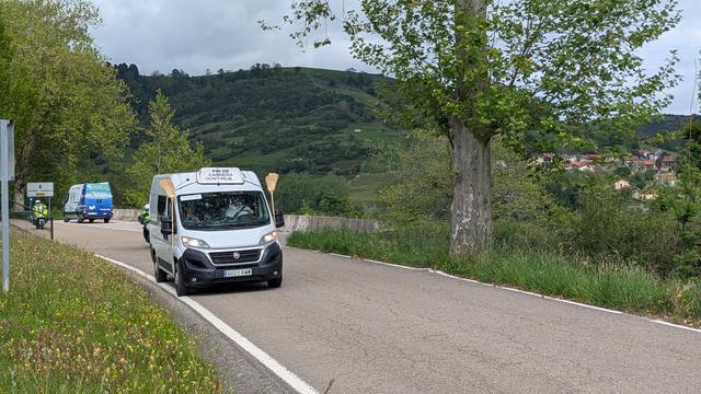 A white van driving up the road after the tail end of the race with sweeping broom in the side of the van, ready to pick up the last cyclist.