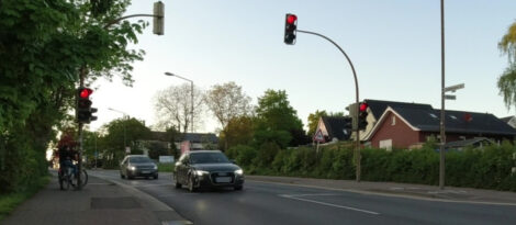 Ein Junge steht an einer Anforderungsampel, um die Straße zu queren. Die Ampel ist gerade auf rot umgesprungen. Ein PKW befindet sich zu diesem Zeitpunkt mitten auf der Querung, der folgende PKW ist ca. 2 Meter von der Haltelinie entfernt.